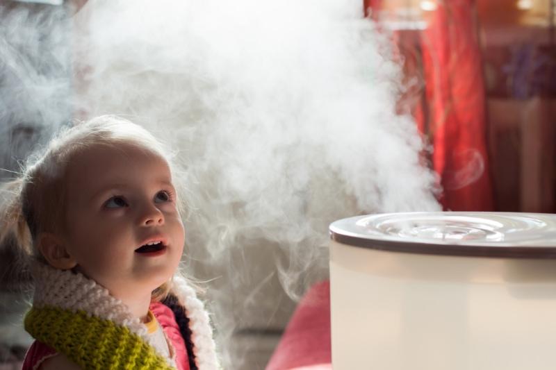 Benefits of Using a Humidifier in Your Home. Image is a photograph of a baby girl looking mystified by a humidifier.